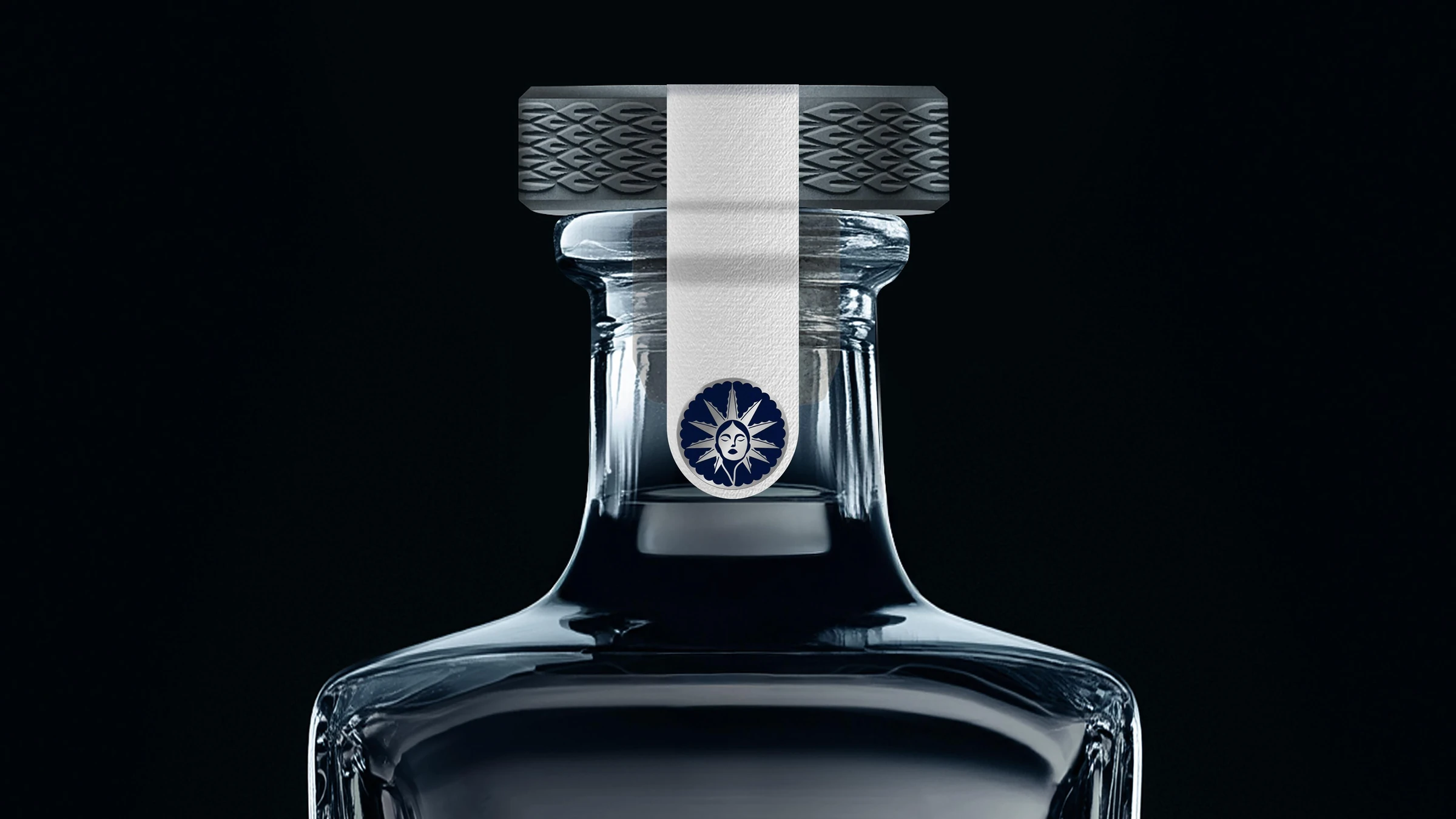 Cuello de la botella del Blanco: tapón gris con relieve tejido, cinta de papel y emblema azul y plata con un rostro al centro de un sol